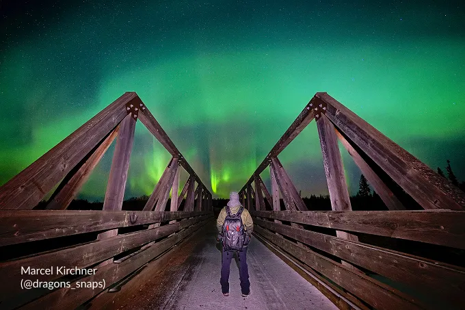 A photographer on a wooden bridge under the northern lights