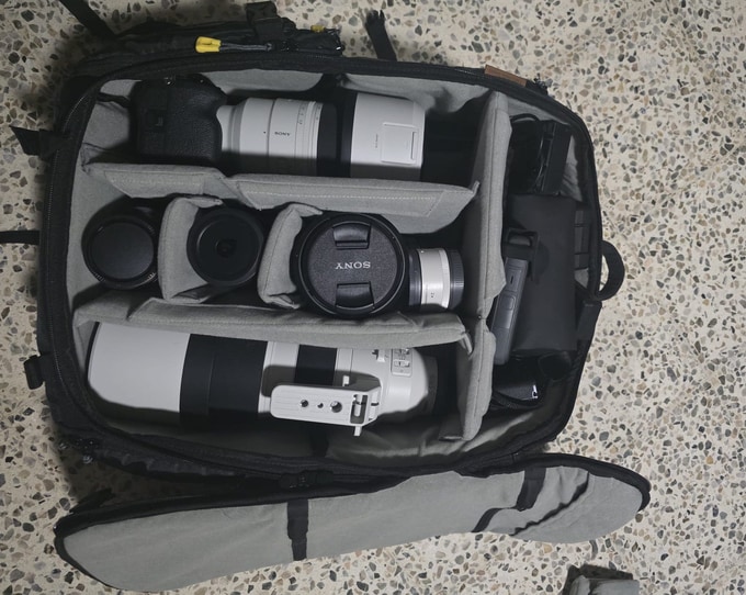 Jamie Cols's bag opened from above: a camera body with a white telephoto lens, other lenses and accessories in the dividers